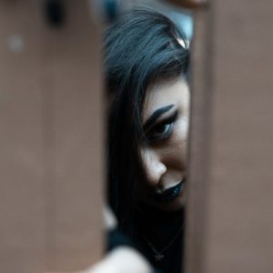 Woman wearing gothic makeup including black lipstick and winged eyeliner looks through a gap