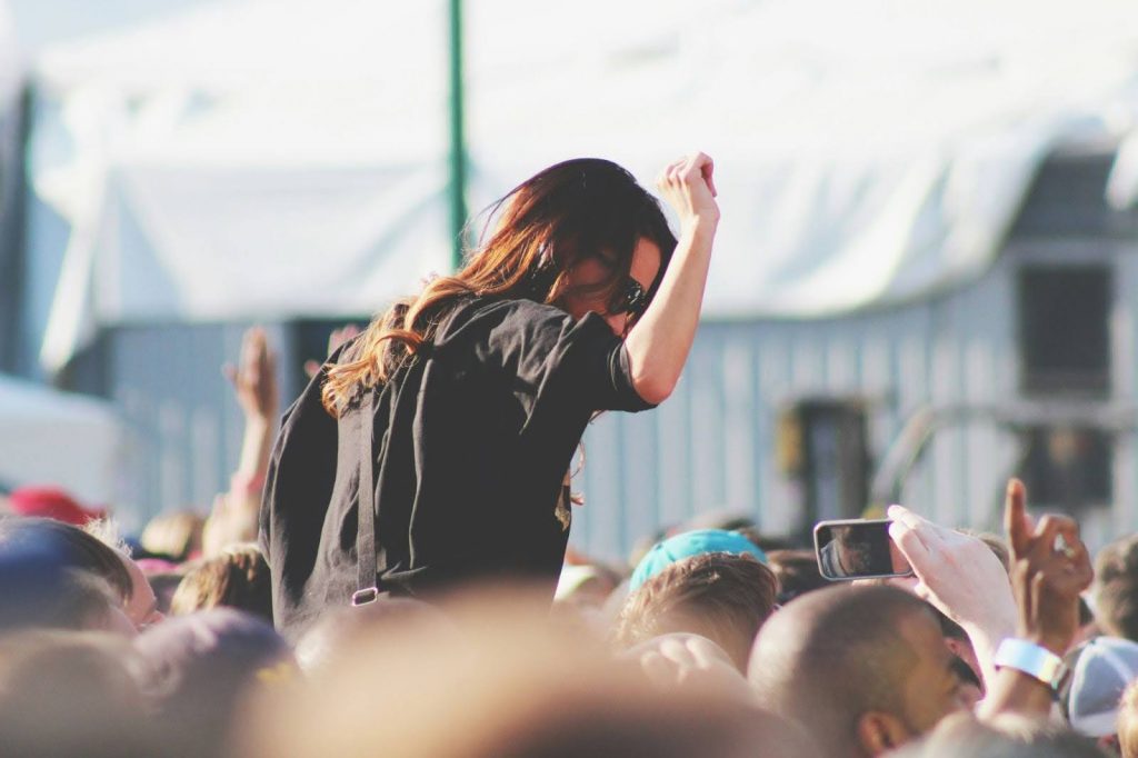 a dark haired woman wearing sunglasses on someone's shoulders in the festival crowd.